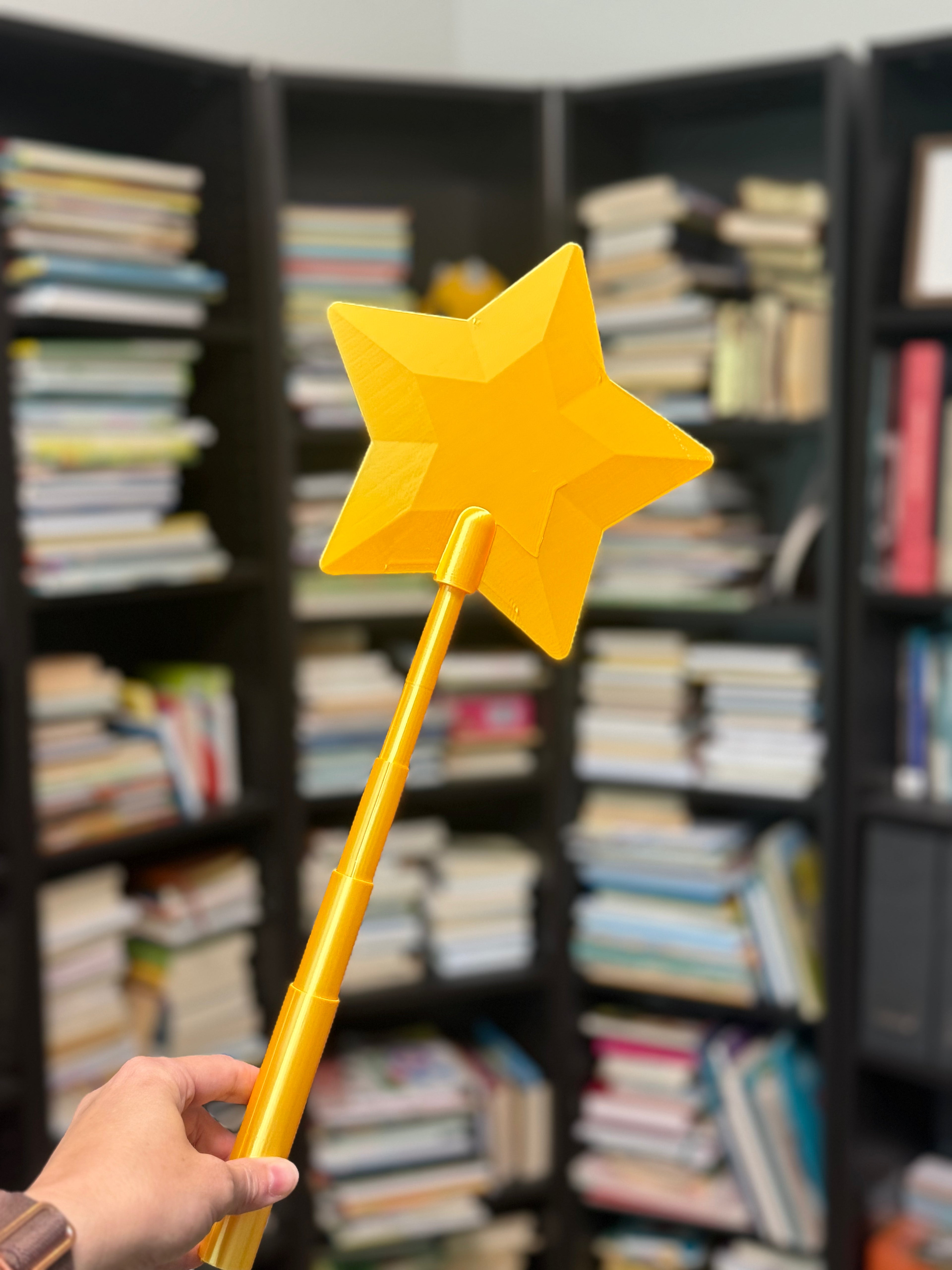 Yellow star-shaped wand held in front of a bookshelf filled with books