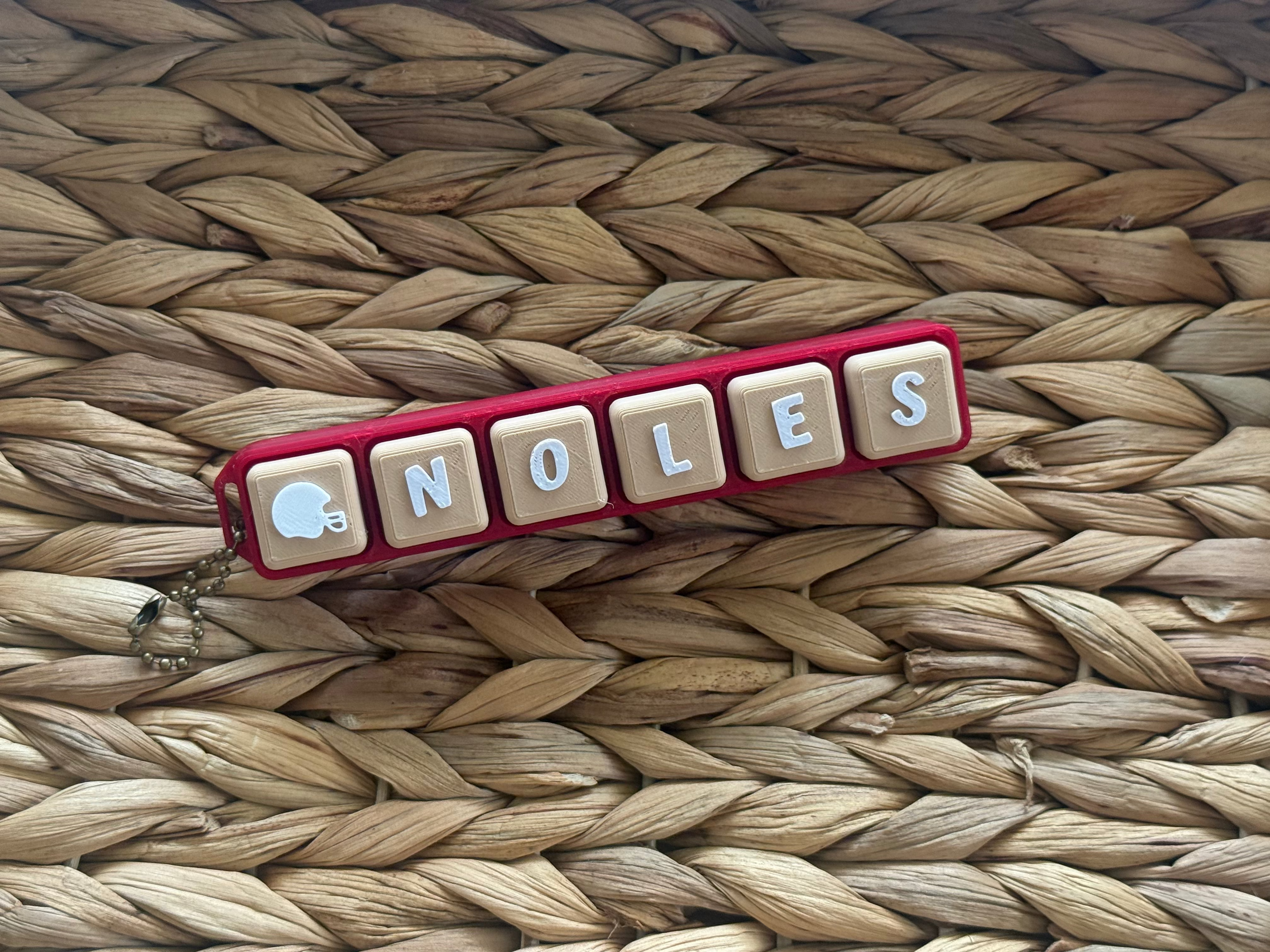 Keychain with letter tiles spelling 'NOLES' on a woven surface