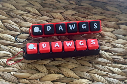 Two keychain designs with 'DAWGS' text on a woven surface