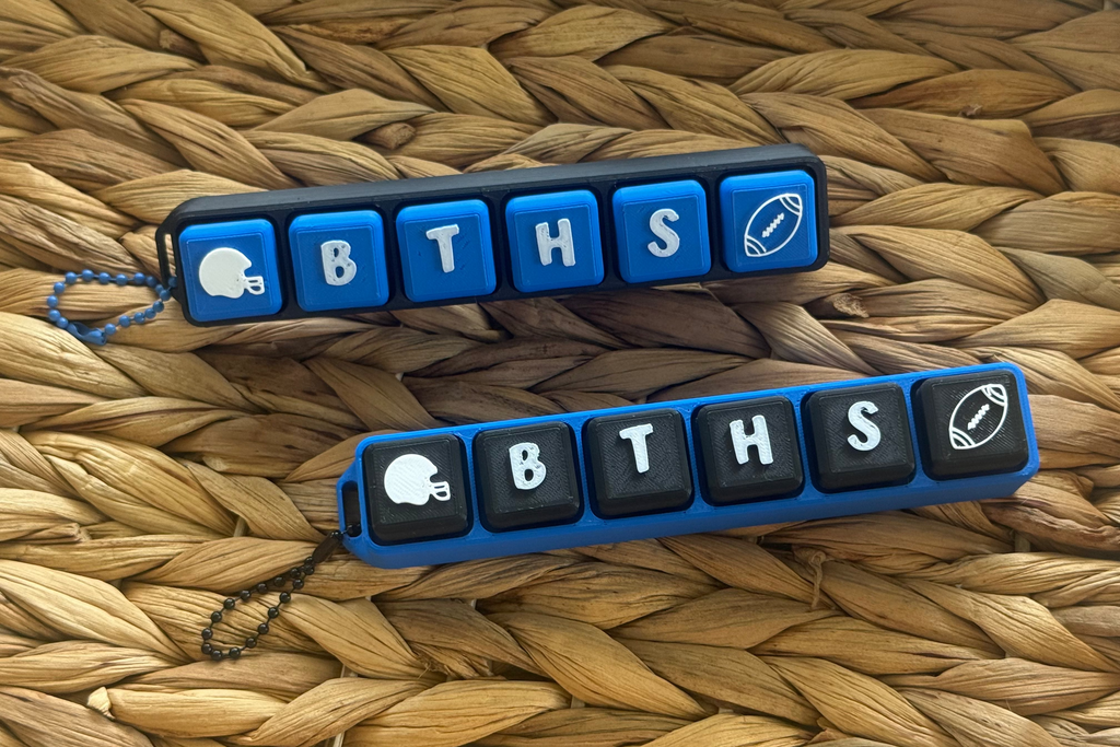 Two blue and black keychains with 'BTHS' letters on a woven surface