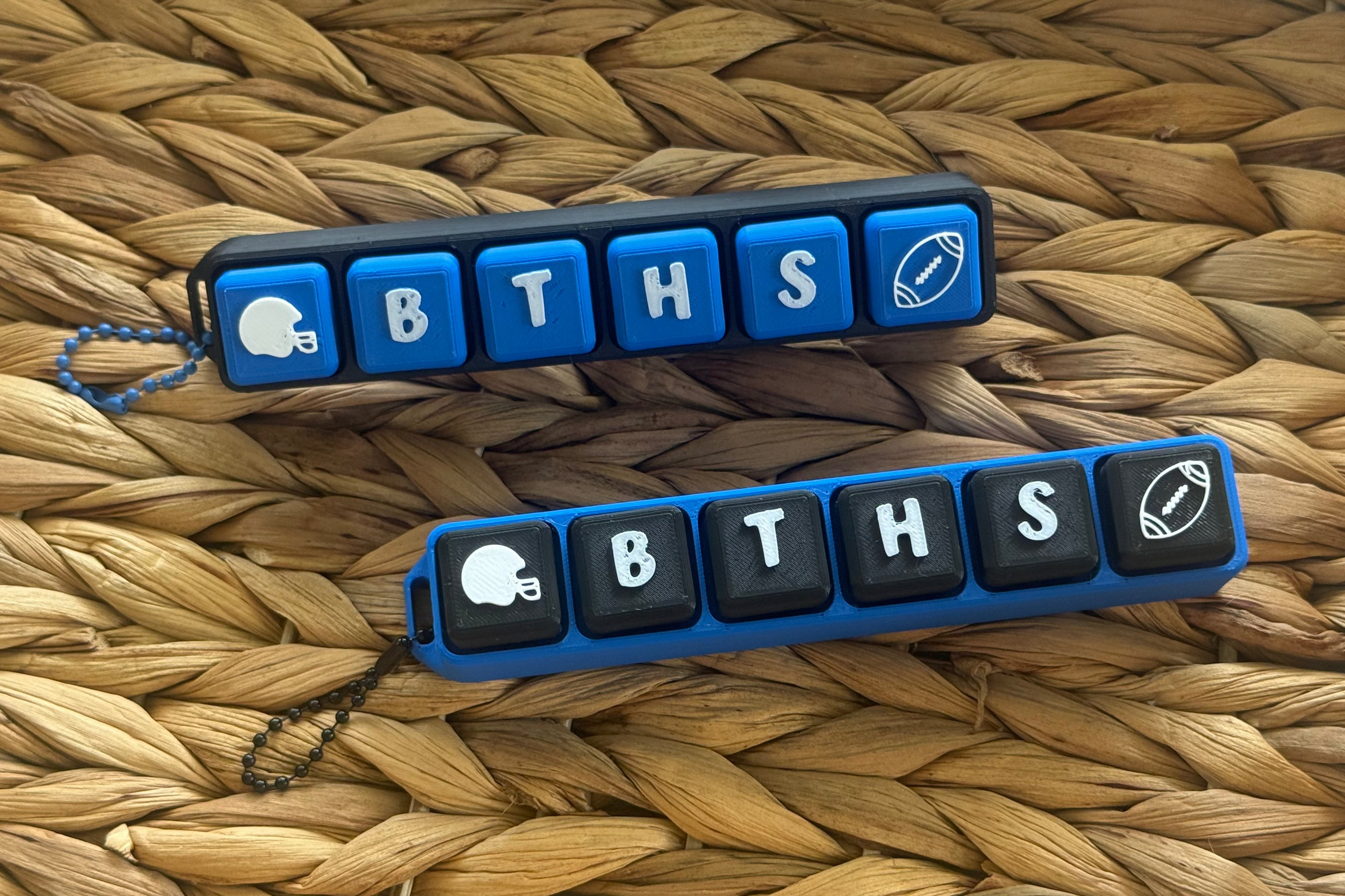 Two blue and black keychains with 'BTHS' letters on a woven surface